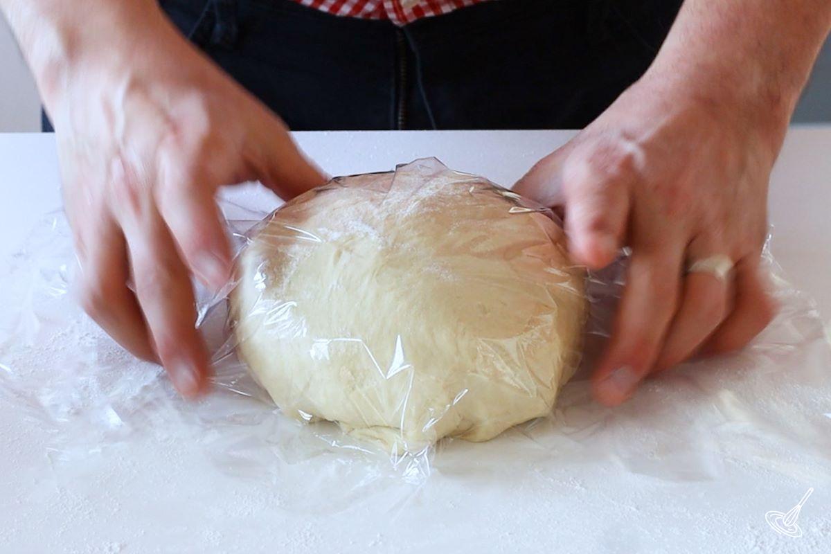 Someone placing plastic wrap on top of a ball of bread dough.