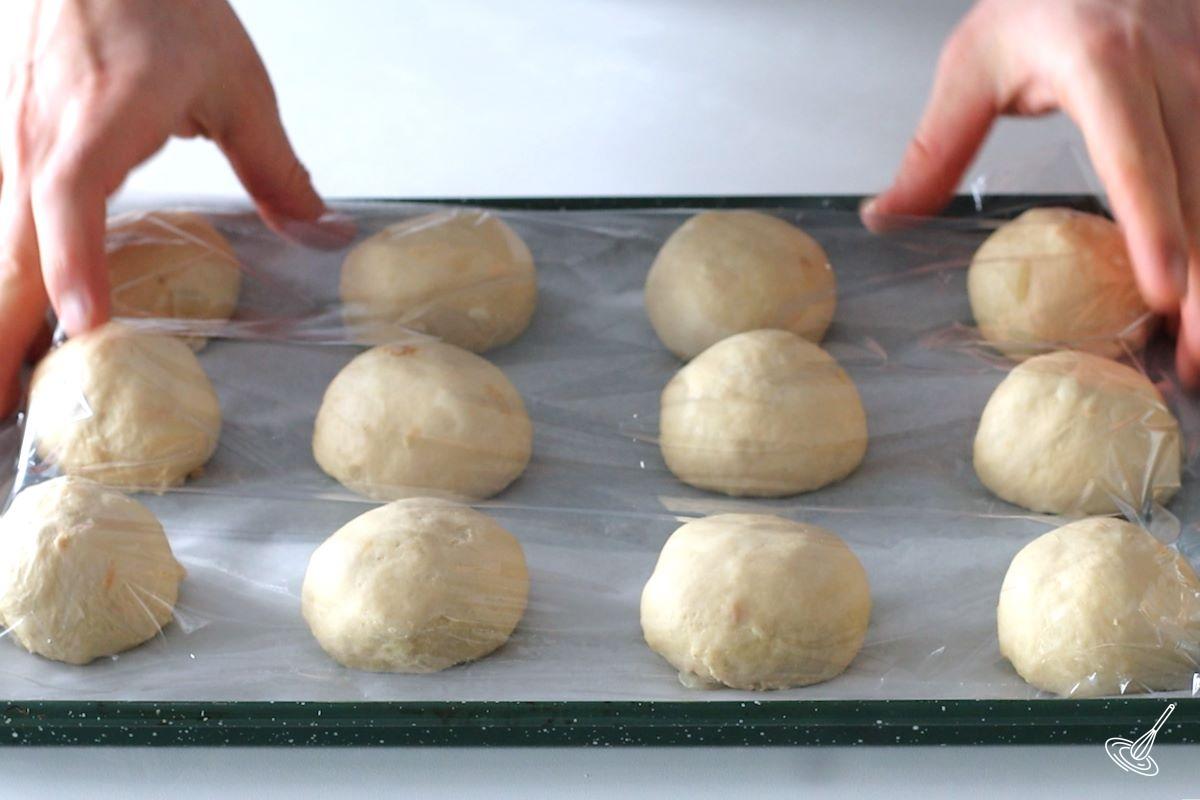 Someone covering a tray of onion rolls with plastic wrap.