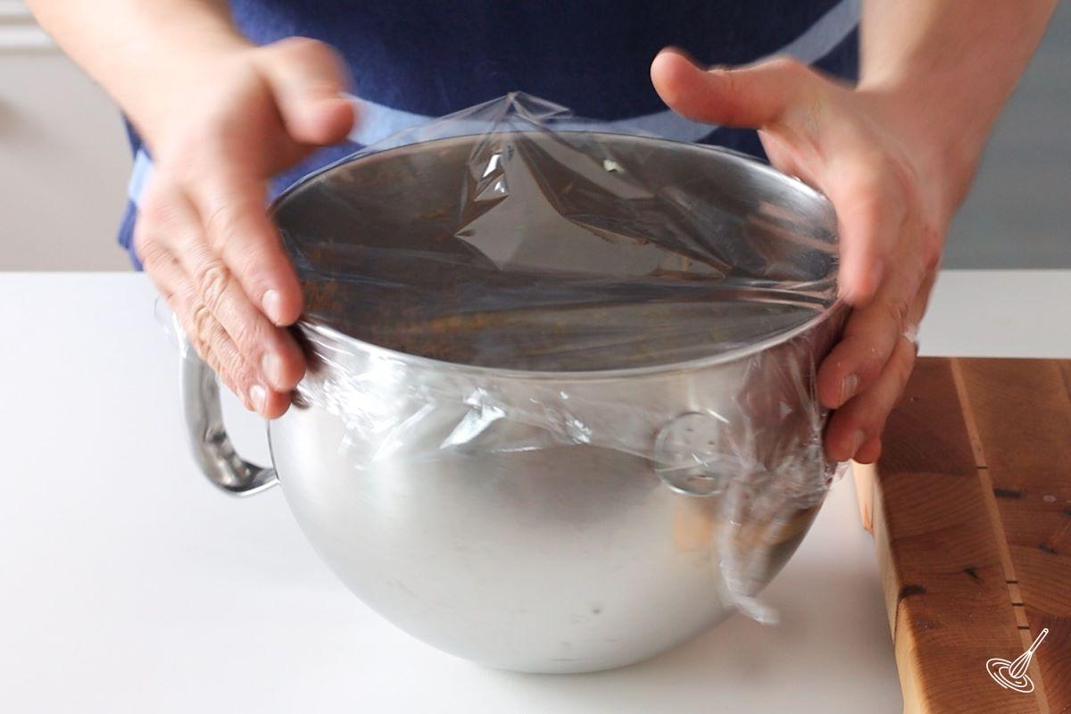 Someone placing plastic wrap on a bowl of a stand mixer.