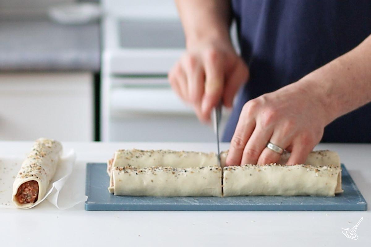 Someone cutting sausage rolls in smaller pieces. 