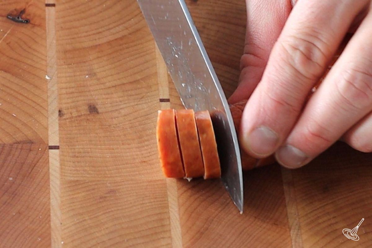 Someone cutting a ¾ piece of sausage.