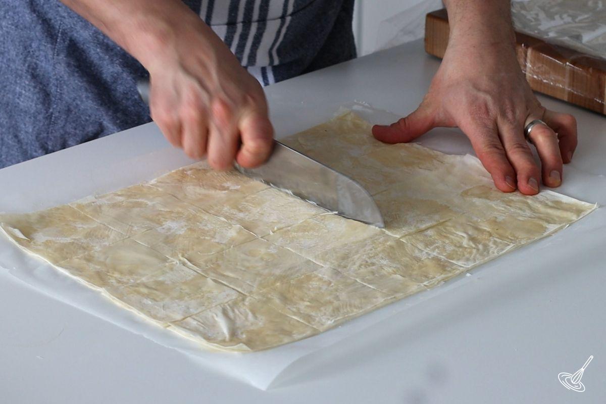 Someone cutting squares of layered butter phyllo dough.