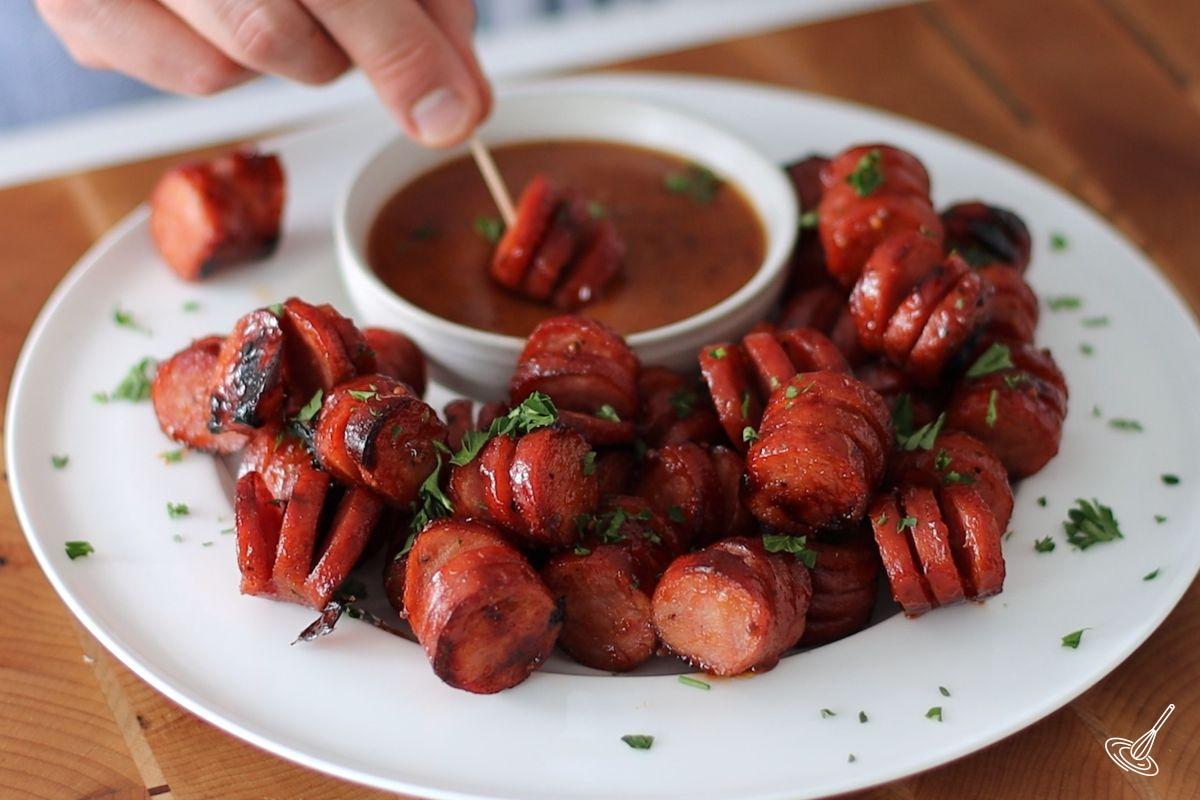 Someone dipping a Maple BBQ Hasselback Kielbasa Bite into a sauce.