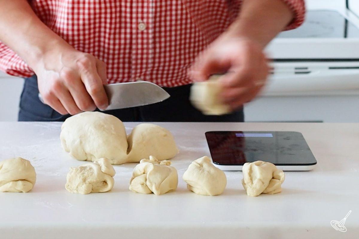 Someone using a knife to portion pieces of bread dough.