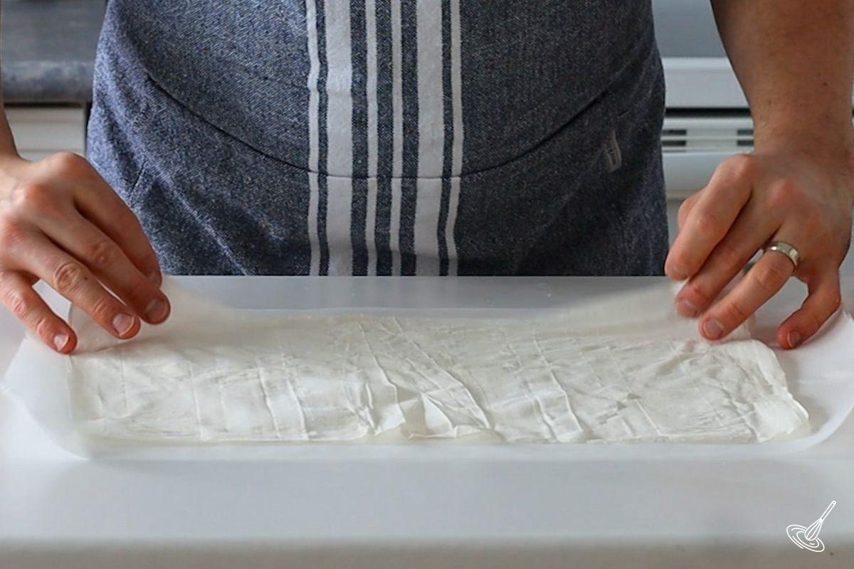 Someone placing a sheet of phyllo pastry on a counter.