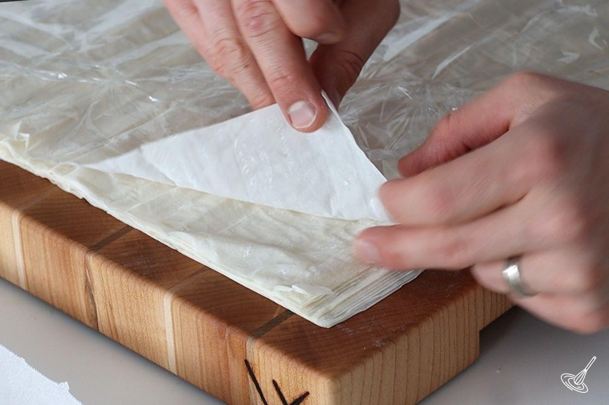 Someone carefully lifting up a sheet of phyllo pastry. 