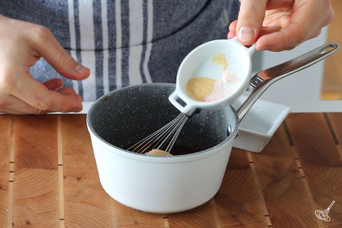 Someone adding salt and garlic powder to a small saucepan.