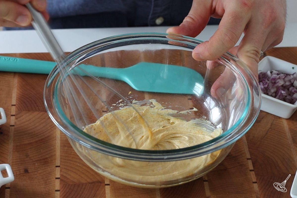 Someone whisking curry mayonnaise in a bowl.