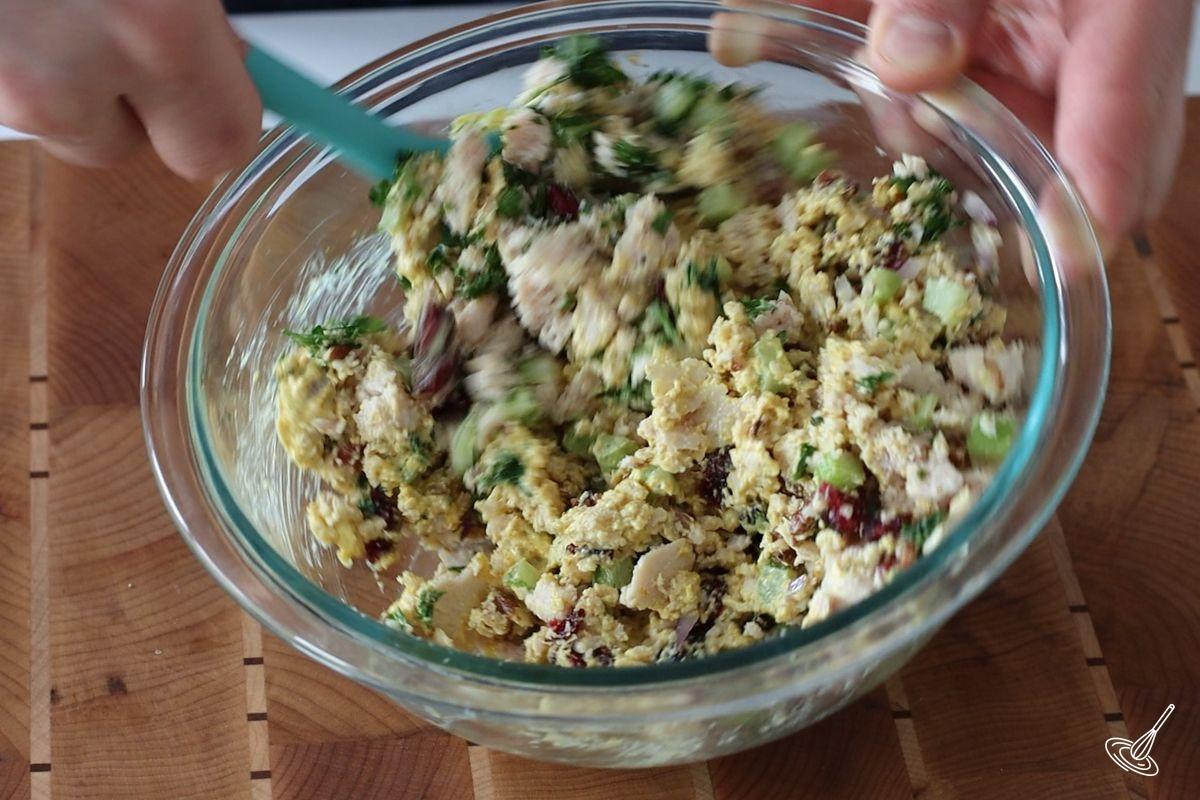 Someone stirring curry chicken salad with a spatula.