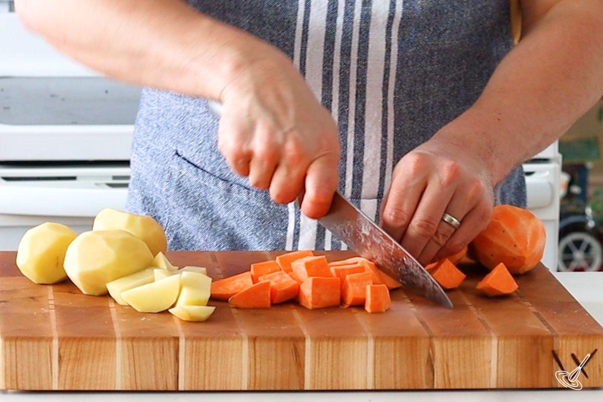 Someone cutting sweet potatoes into cubes. 