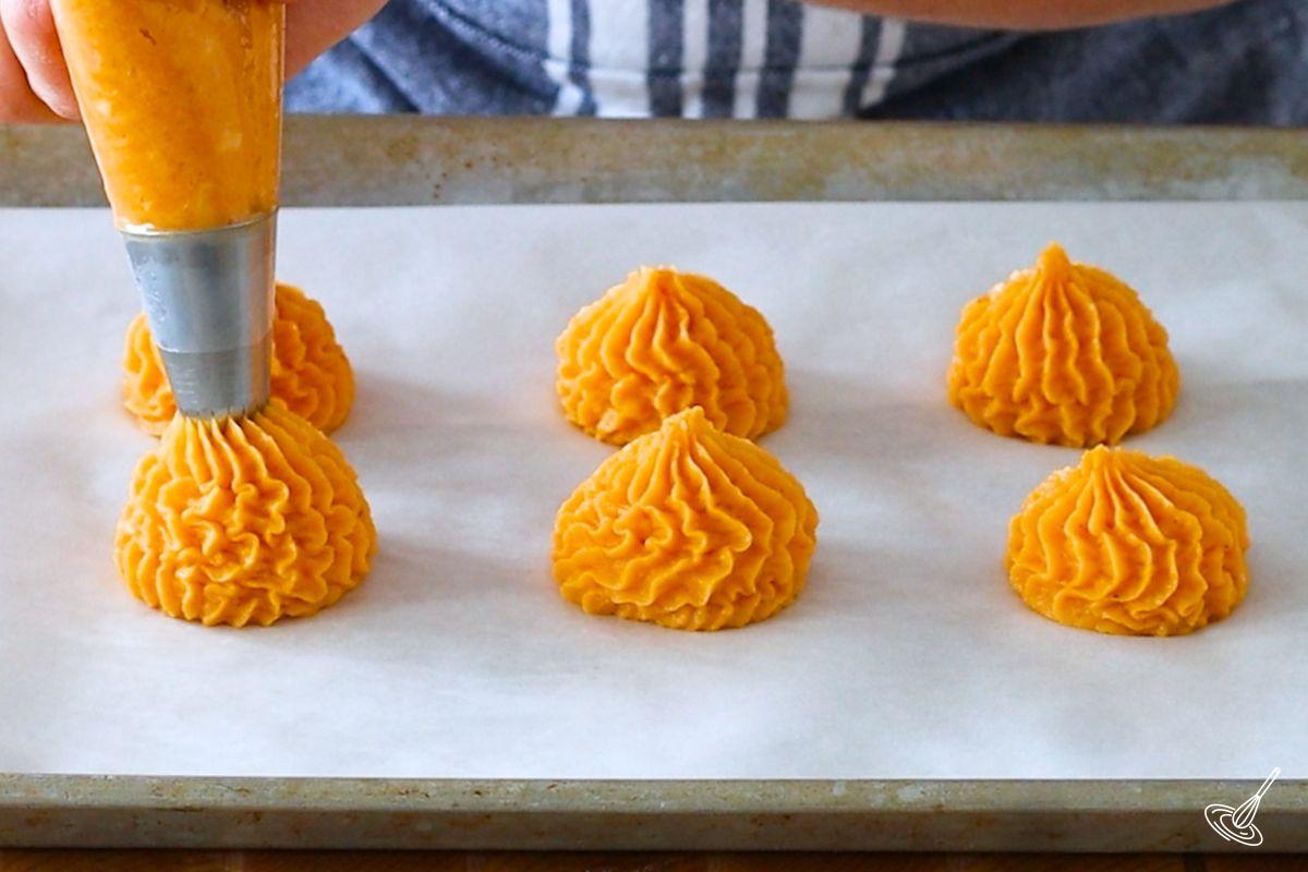 Someone piping the duchess sweet potatoes on a baking tray.