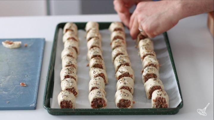 Someone placing french onion sausage rolls on a baking tray. 