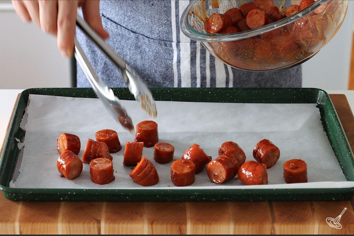 Someone placing Maple BBQ Hasselback Kielbasa Bites on a baking tray.