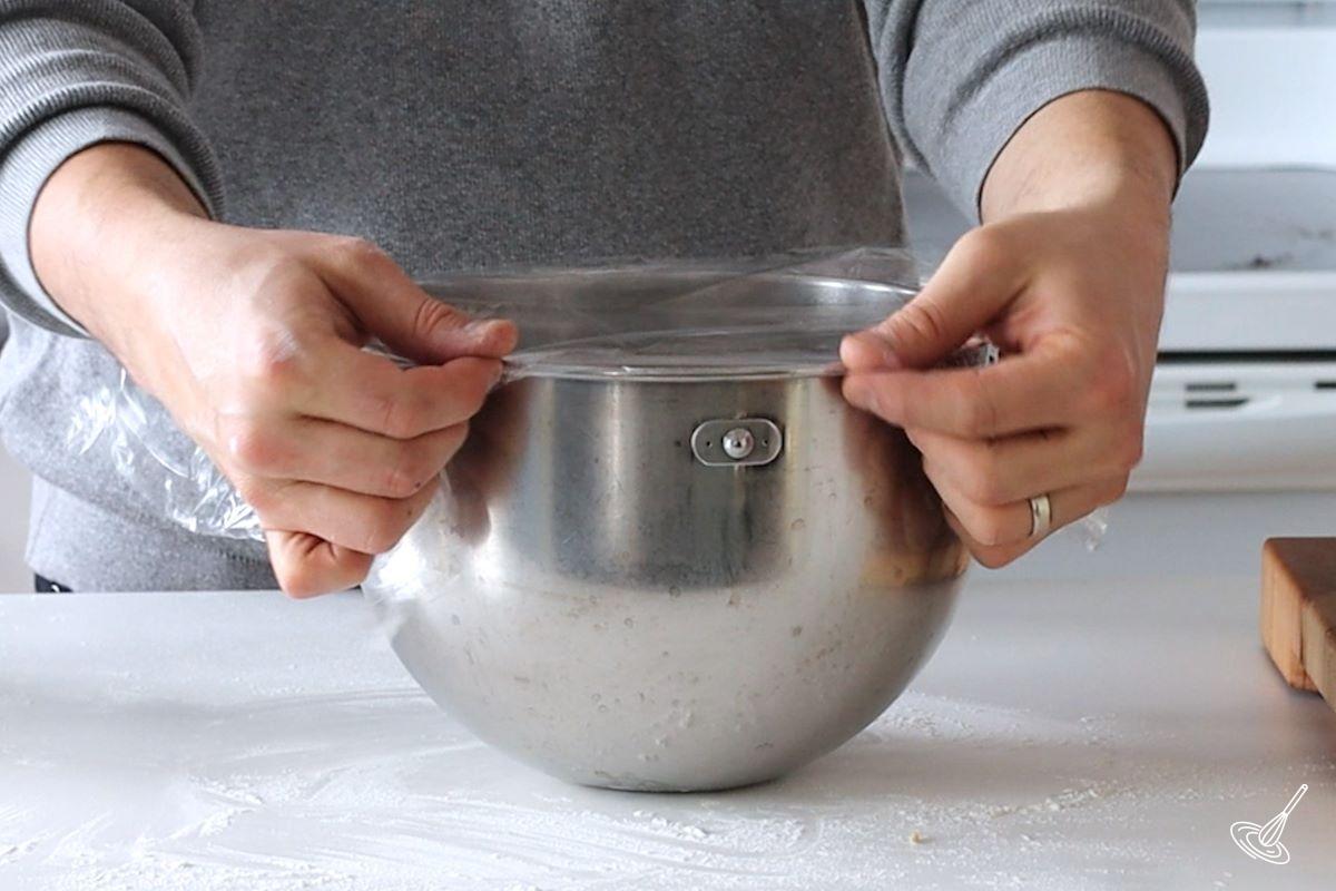 Someone placing plastic wrap over the bowl of a stand mixer