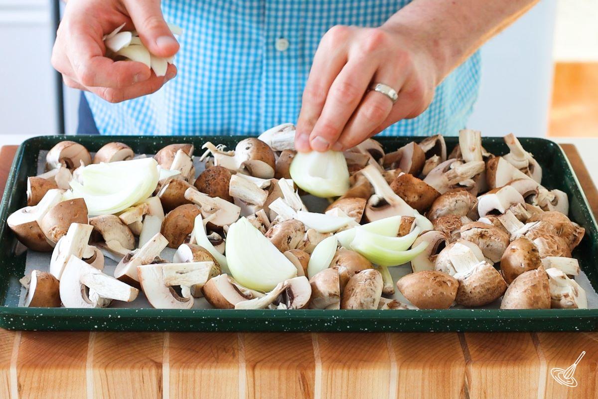 Someone placing chopped vegetables on a baking tray.