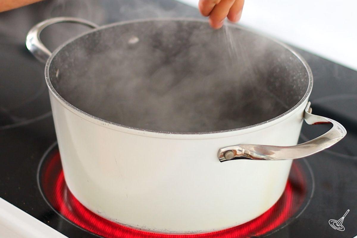 Someone adding salt to a large pot of boiling water. 