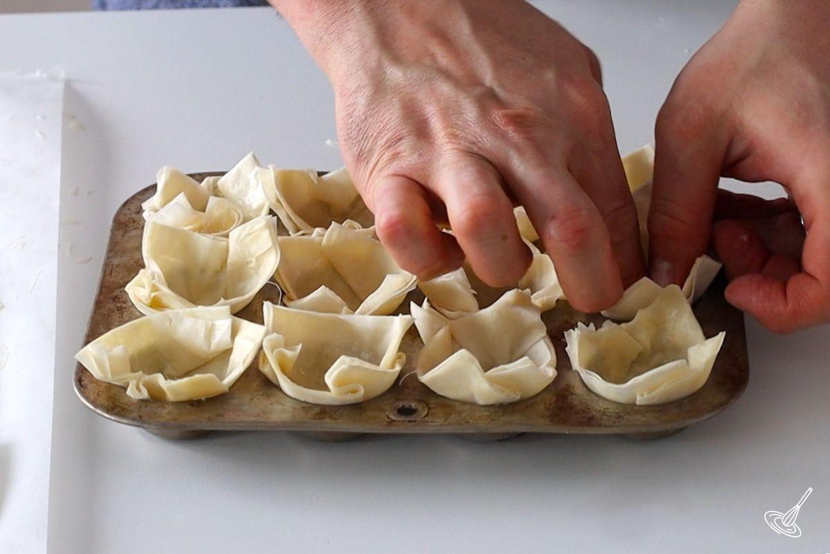 Someone placing mini phyllo cups in a mini muffin tin.