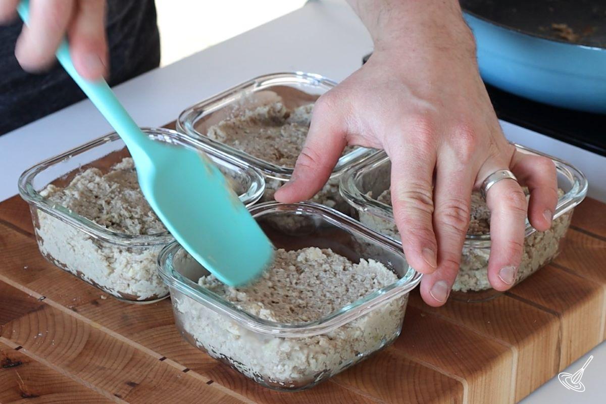 Someone using a rubber spatula to flatten out cretons in containers.