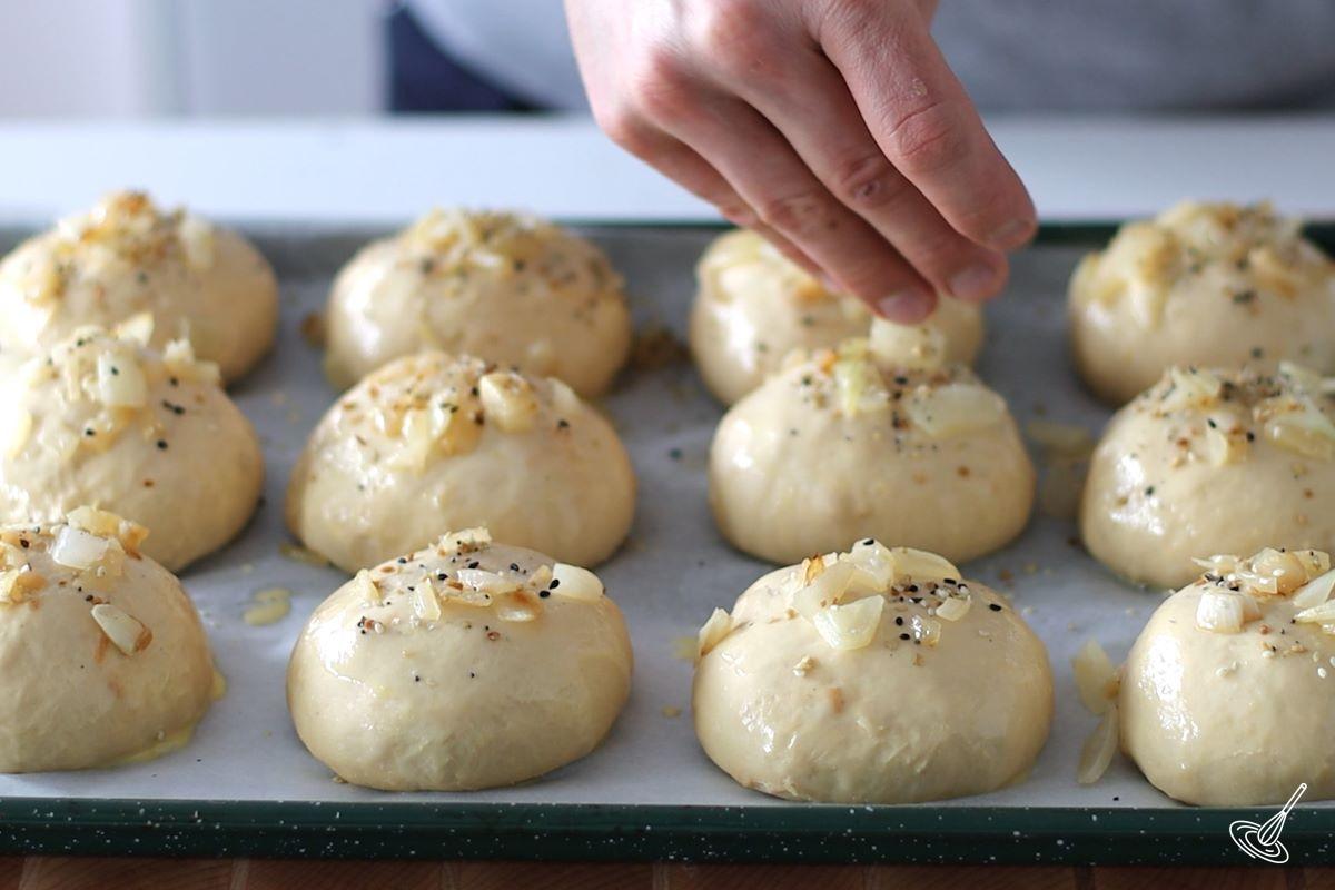 Someone sprinkling seasoning on onion rolls.