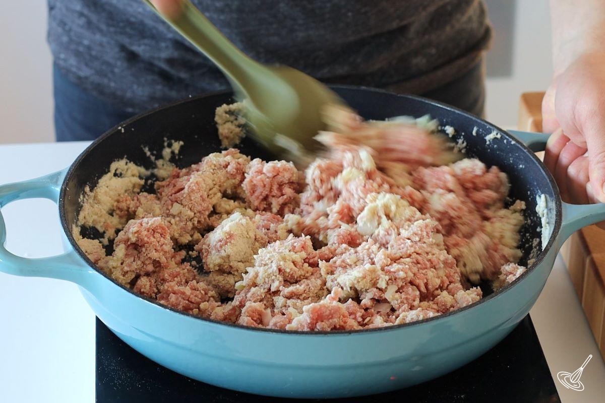 Someone stirring the ingredients for a cretons recipe in a large skillet.