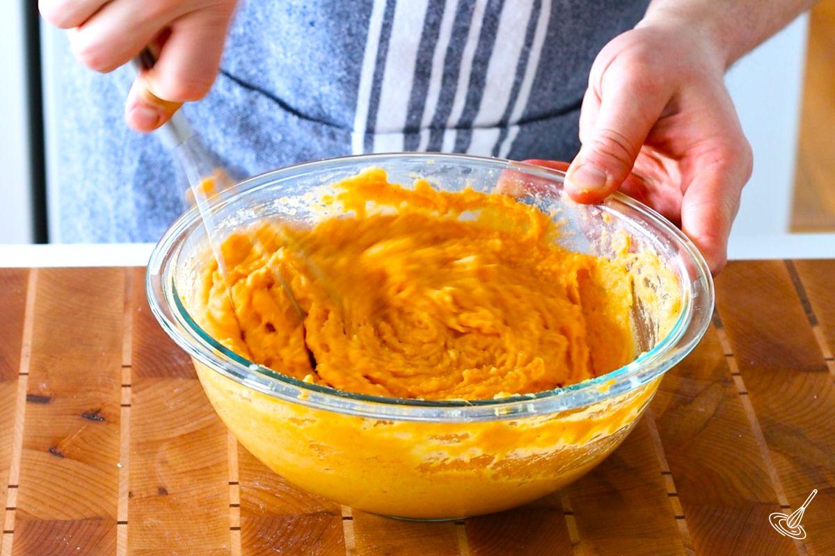 Someone using a whisk to mix the duchess sweet potatoes mixture.