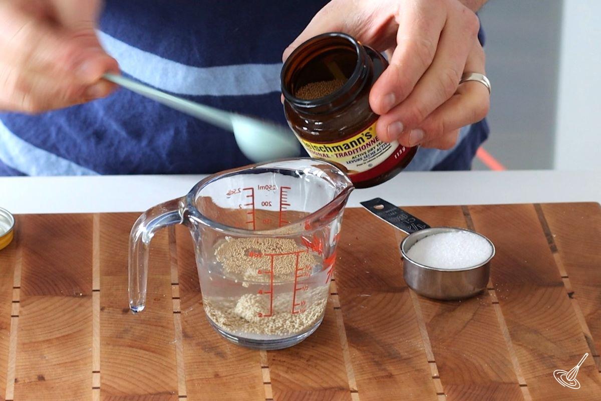 Someone adding yeast to a measuring cup. 