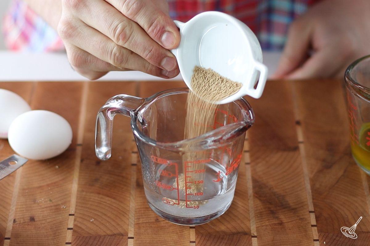 Someone adding active dry yeast to warm water.