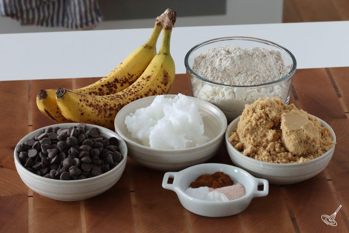 Ingredients to make Vegan Banana Chocolate Chip Cookies, including flour, coconut oil, chocolate chips, and bananas.