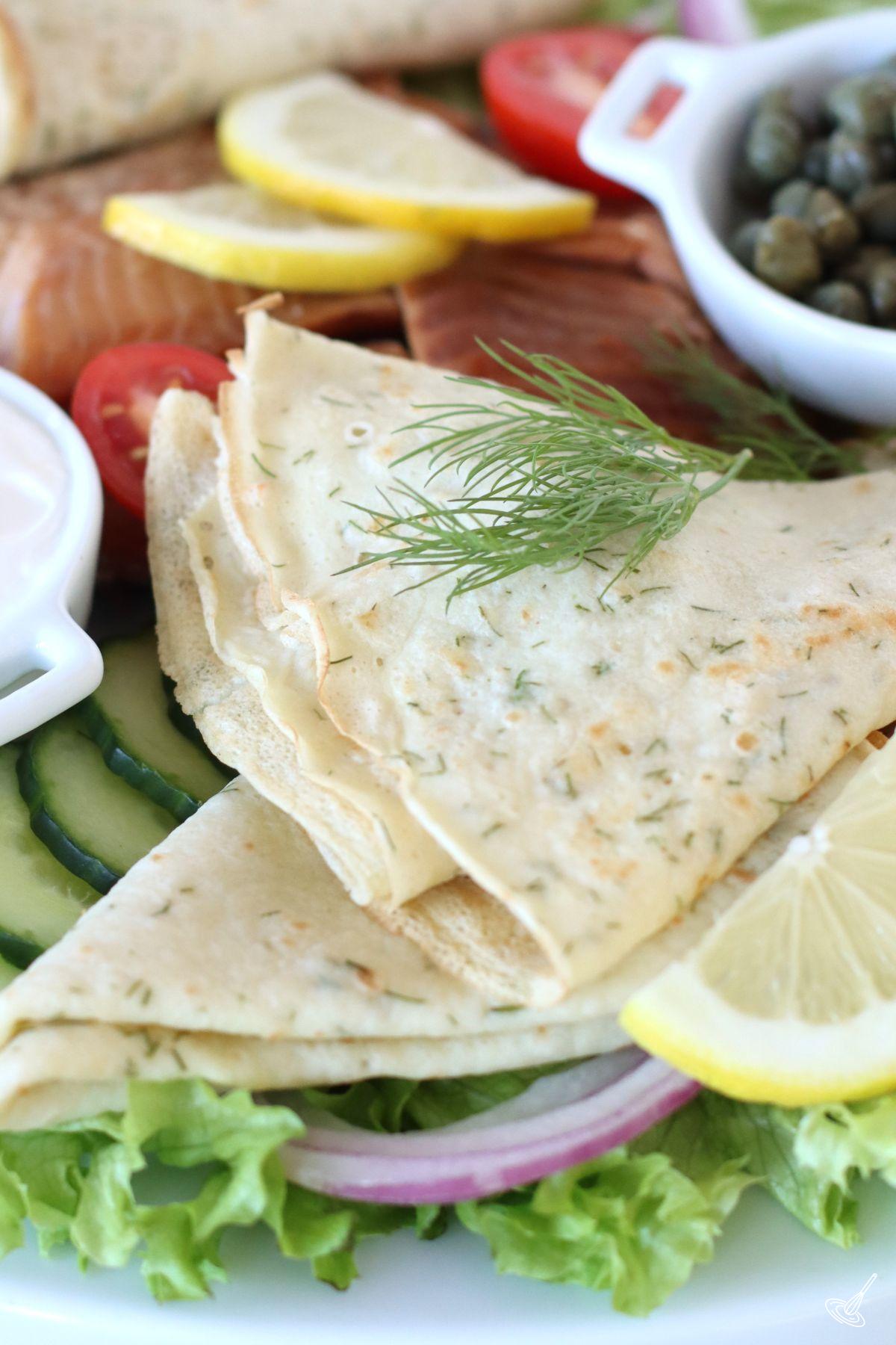 Dill French Crêpes on a platter with vegetables and smoked salmon.