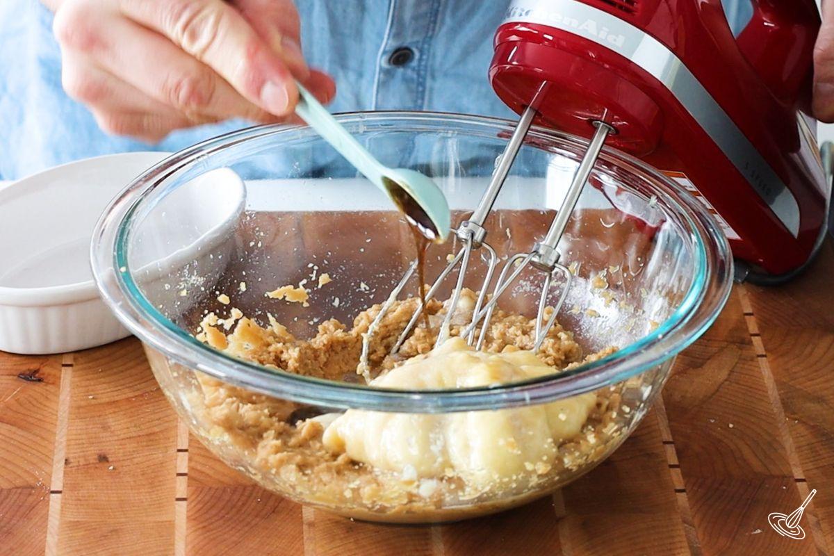 Someone adding vanilla and bananas to a bowl of creamed sugar.