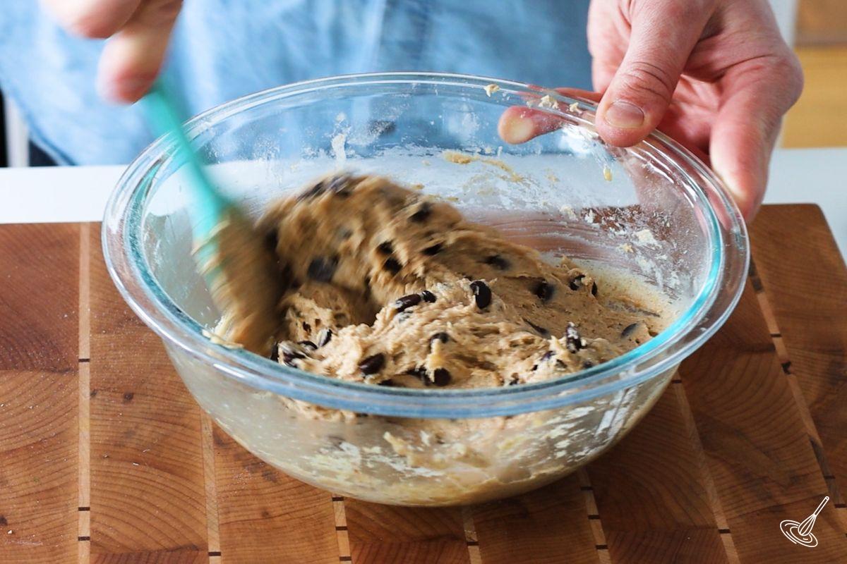 Someone using a rubber spatula to add chocolate chips to Vegan Banana Chocolate Chip Cookie dough.