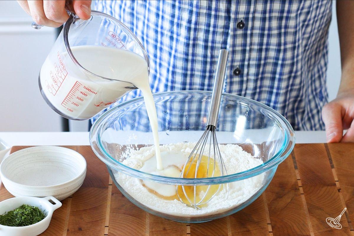 Someone adding milk to a bowl with eggs.