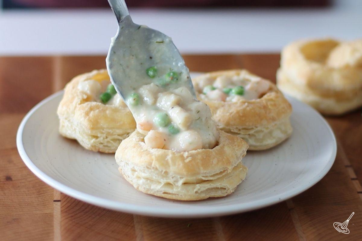 Someone using a spoon to fill the Seafood Vol-au-Vent. 