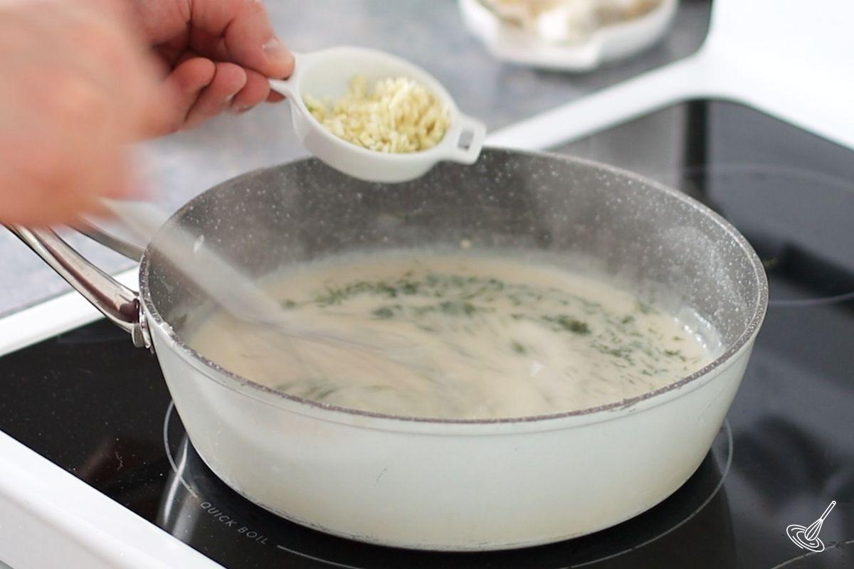 Someone adding garlic and fresh dill to a skillet of bechamel sauce. 