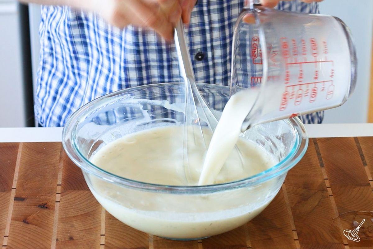 Someone pouring milk into a bowl of Dill French Crêpes batter. 