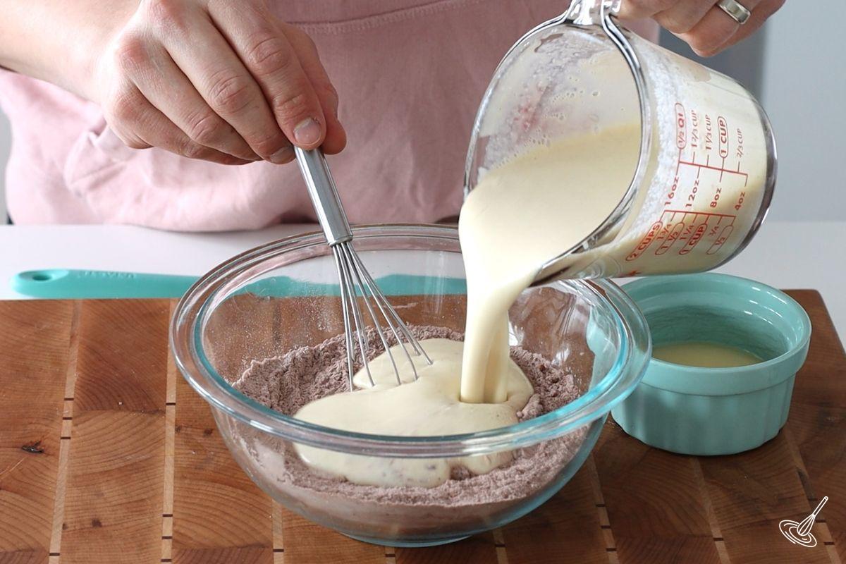 Someone pouring a cottage cheese mixture into a large bowl of flour.
