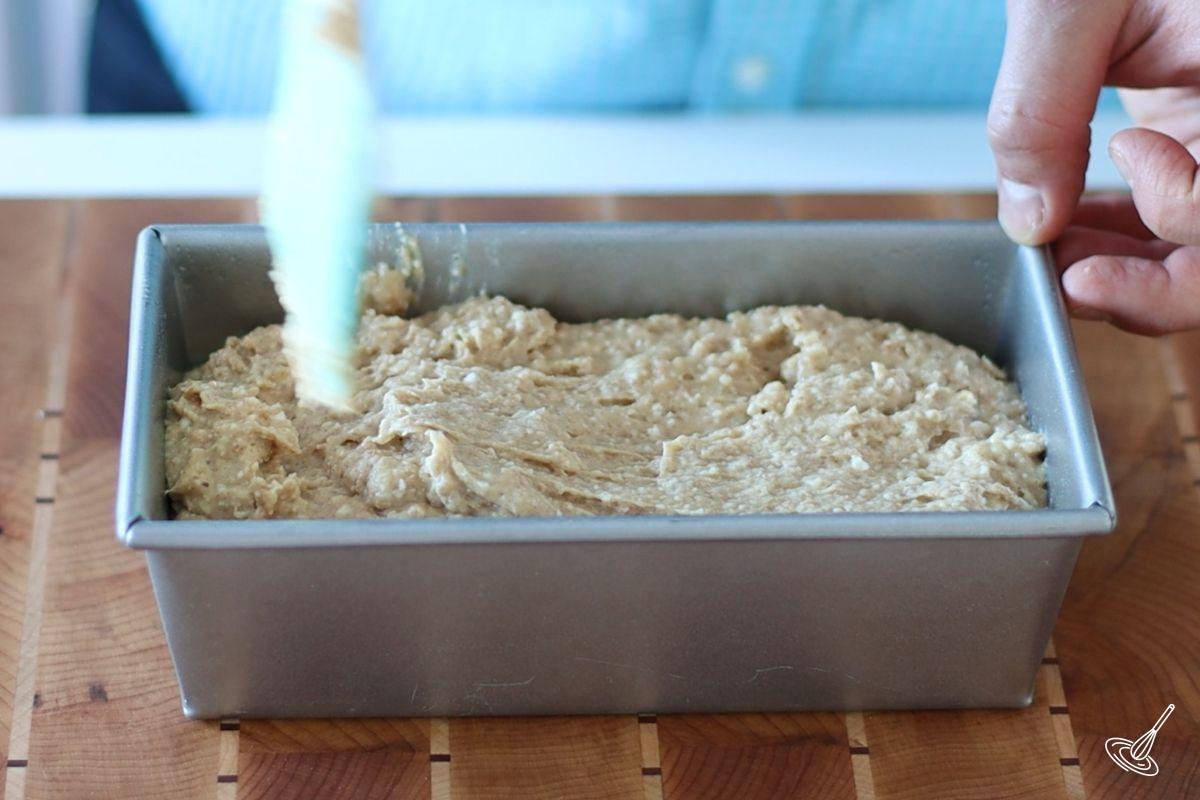 Someone smoothing the top of banana bread in a pan.