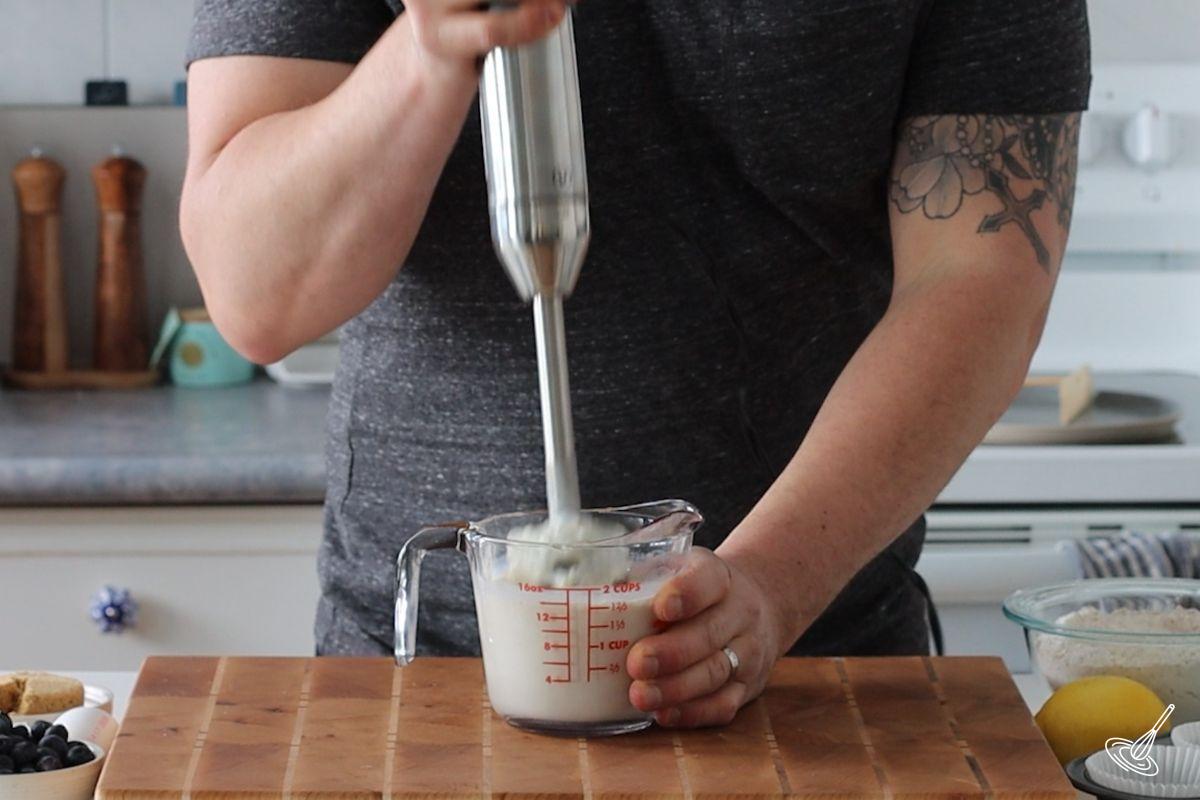 Someone using an immersion blender to puree cottage cheese with milk. 