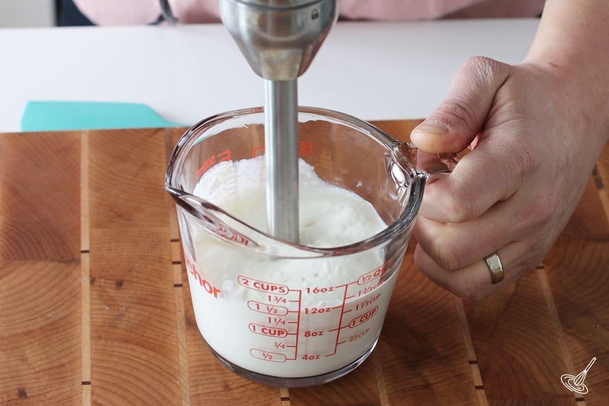 Someone using a stick blender to puree cottage cheese. 