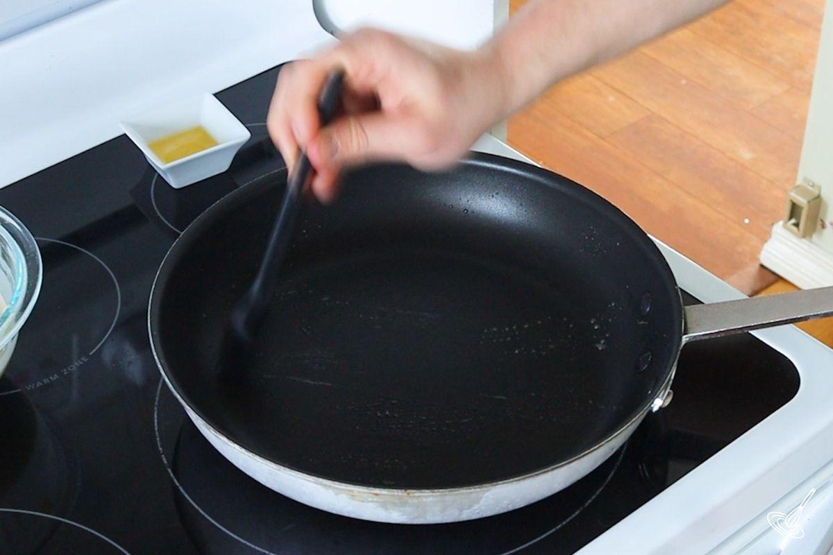 Someone brushing a hot frying pan with melted butter.