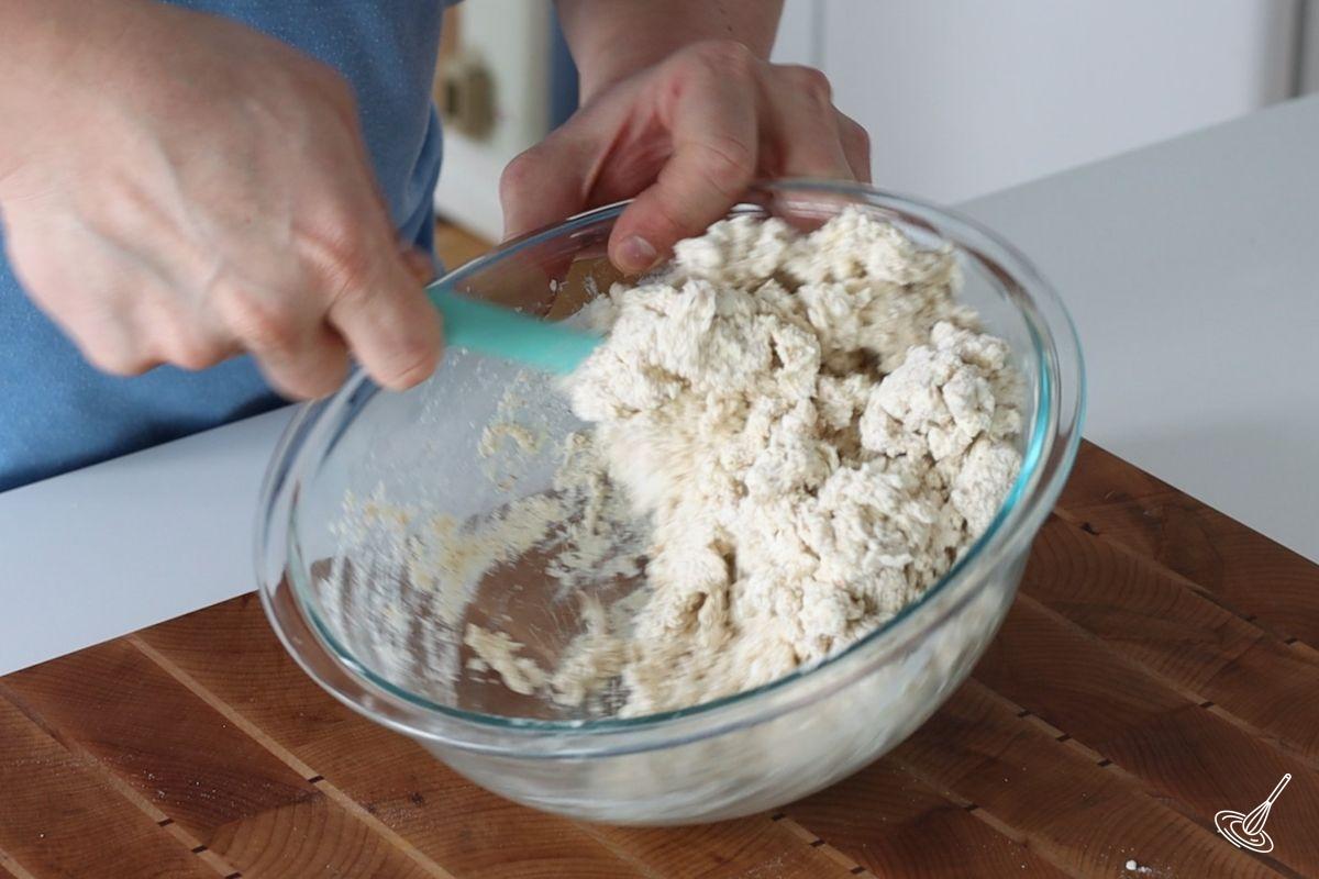 Someone using a rubber spatula to mix cottage cheese biscuits dough. 