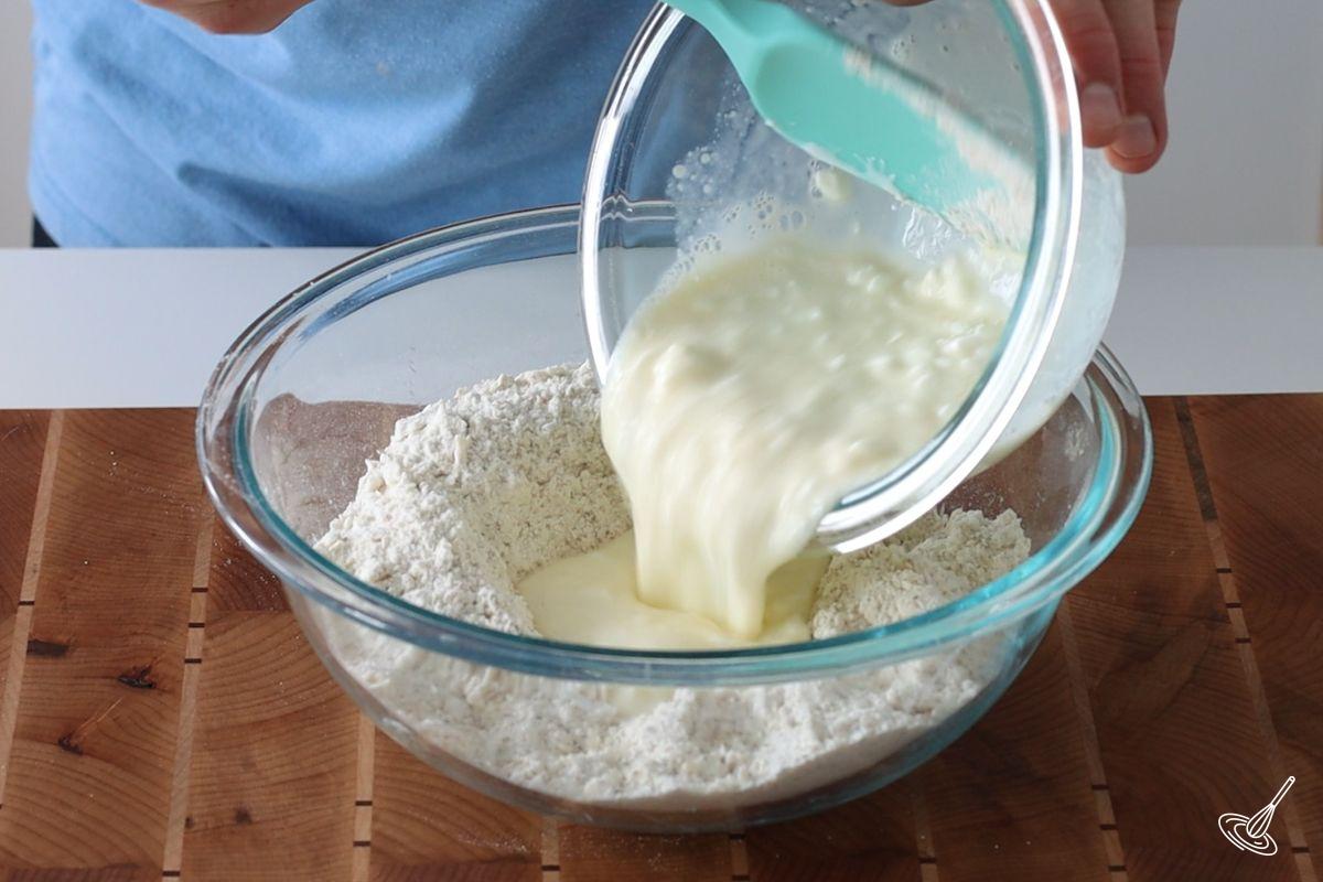 Someone pouring a wet cottage cheese mixture into a larger bowl containing a flour mixture. 