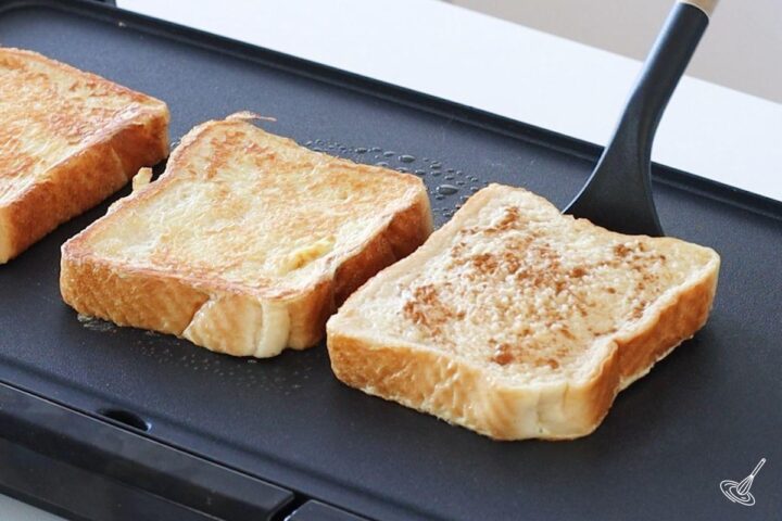 Someone using a spatula to flip a cinnamon vanilla french toast on the griddle.