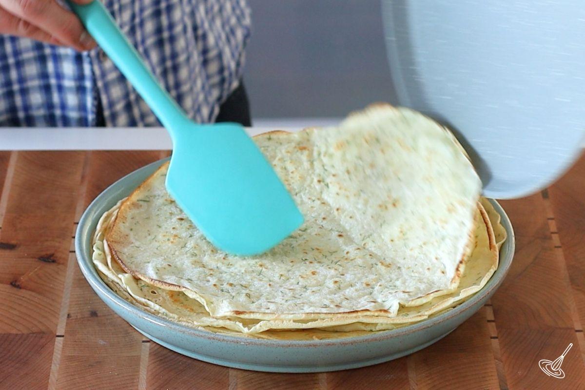 Someone place a cooked Dill French Crêpes on a plate.