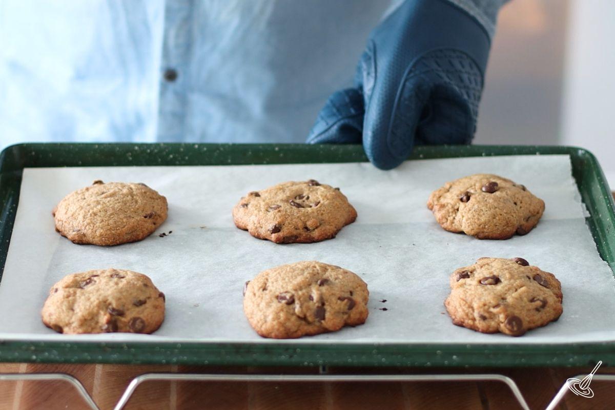 Someone placing a tray of baked Vegan Banana Chocolate Chip Cookies on a cooling rack. 