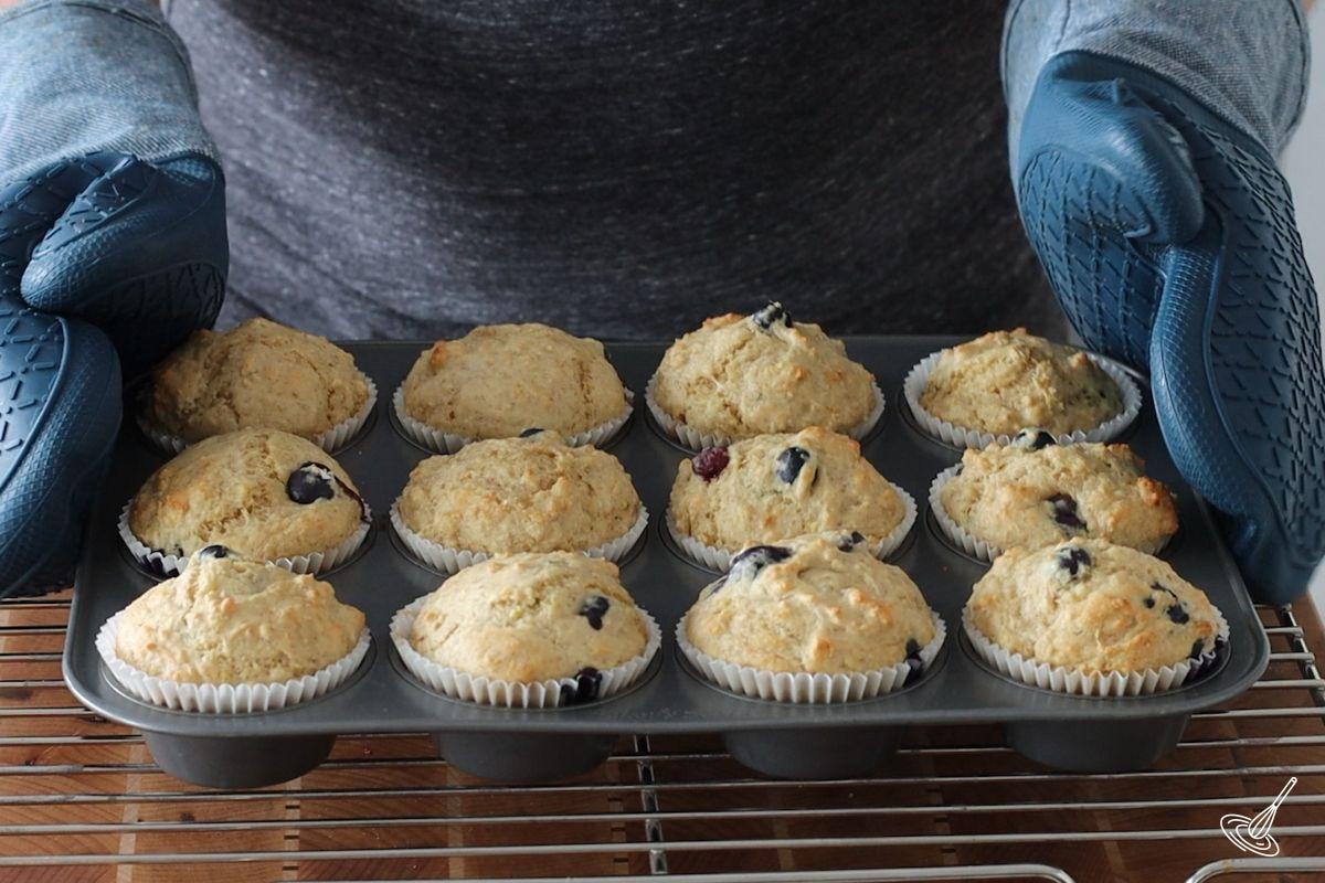 Someone placing baked Cottage Cheese Blueberry Muffins on a cooling rack. 
