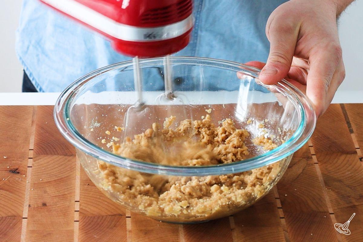Someone using a hand blender to cream together brown sugar and coconut oil.