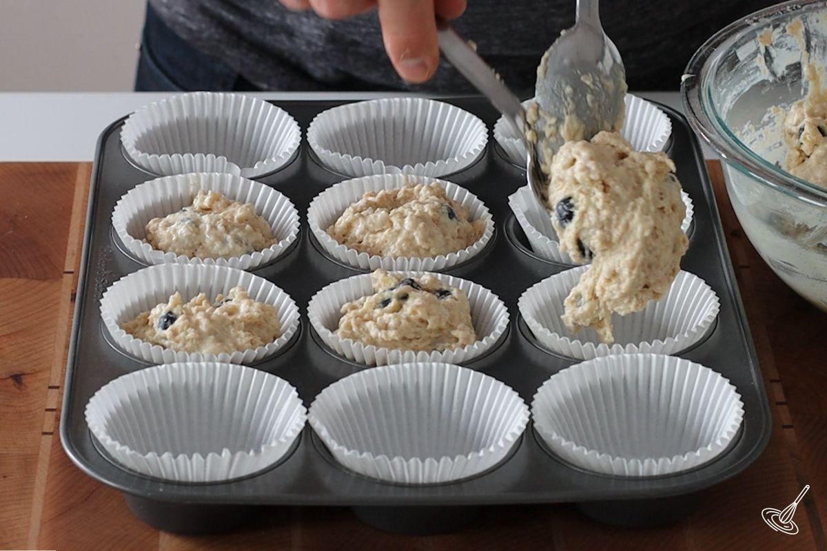 Someone spooning muffin batter in a lined muffin tray.