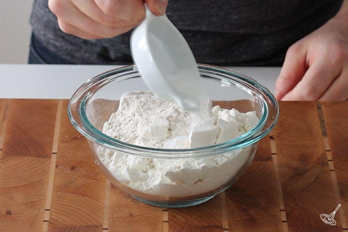 Someone adding dry ingredients in a bowl.