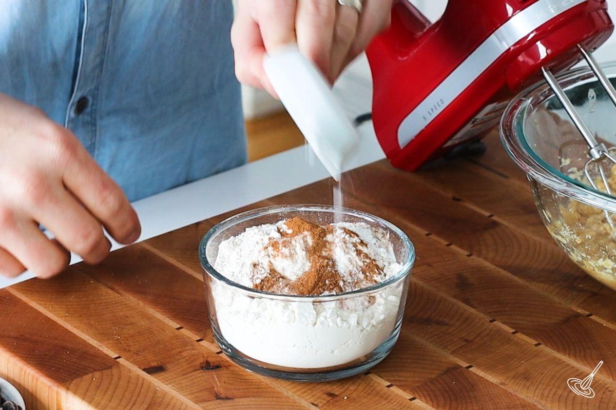 Someone adding cinnamon to a bowl of flour.